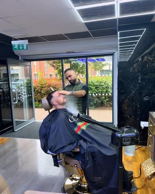 Nwah Trims barber working on a client in the chair by the shop's front windows
