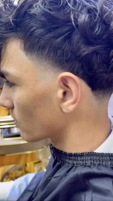 Low taper fade blended into a wavy fringe, side profile, at Nwah Trims